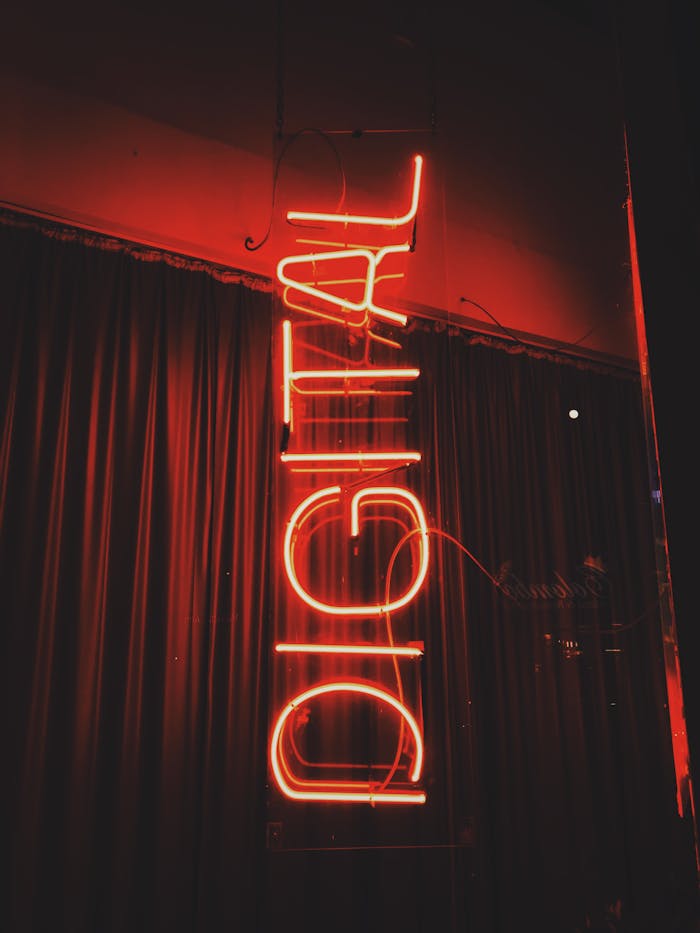 Bright red neon sign with 'Digital' text glowing against a curtain backdrop. Urban night scene.